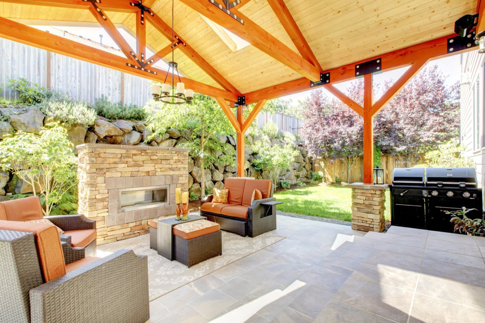 Custom covered patio with stone fireplace and lounge seating by Legado Outdoor Living
